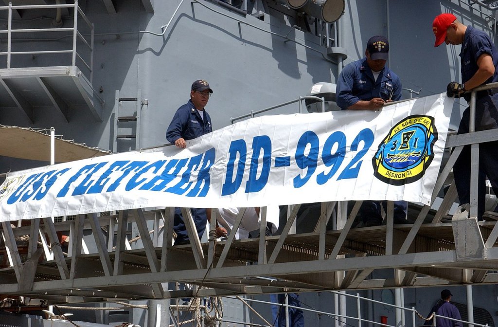 Sailors assigned to the Spruance Class destroyer USS Fletcher (DD 992) attach the ship's banner t...