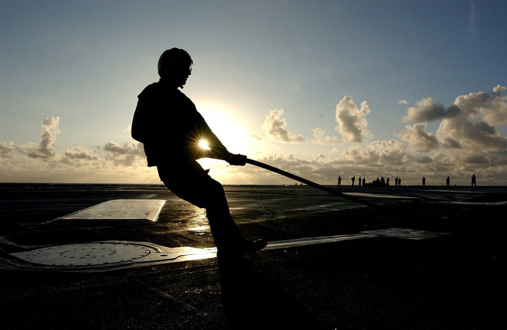 An Aviation Boatswain's Mate prepares to rig an arresting gear wire in preparation for early morn...