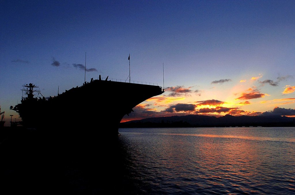 The sun sets behind the Nimitz-class nuclear powered aircraft carrier USS John C
